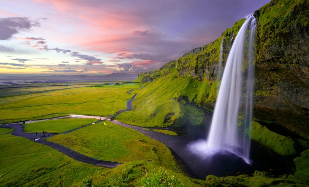 Iceland travel costs 2026 — Seljalandsfoss waterfall with green hills and dramatic sky | tripbudgetcalculator.com