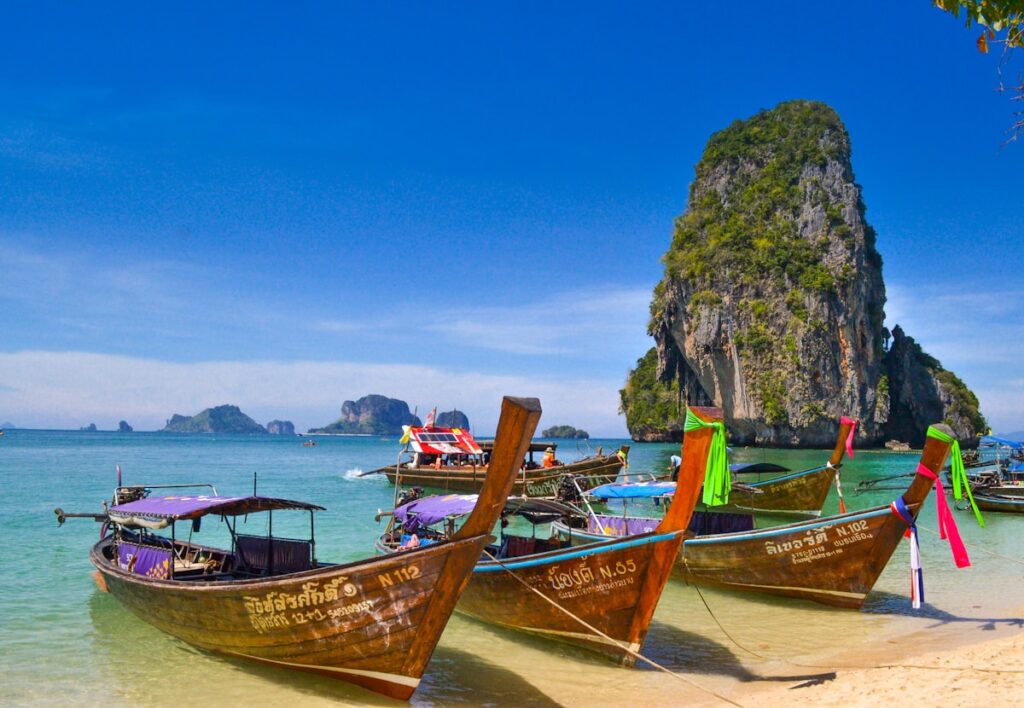 Thailand travel costs 2026 — colorful longtail boats on Railay Beach with limestone karsts | tripbudgetcalculator.com